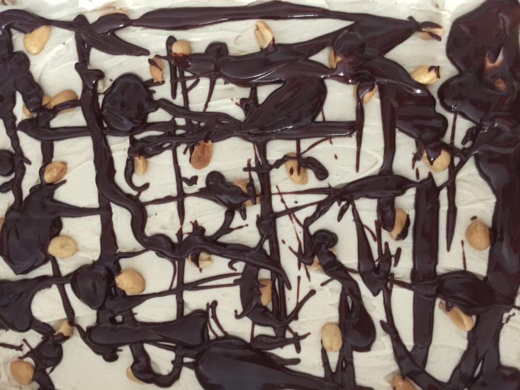 Image of a melted chocolate and whole peanuts on top of a no bake peanut butter cheesecake