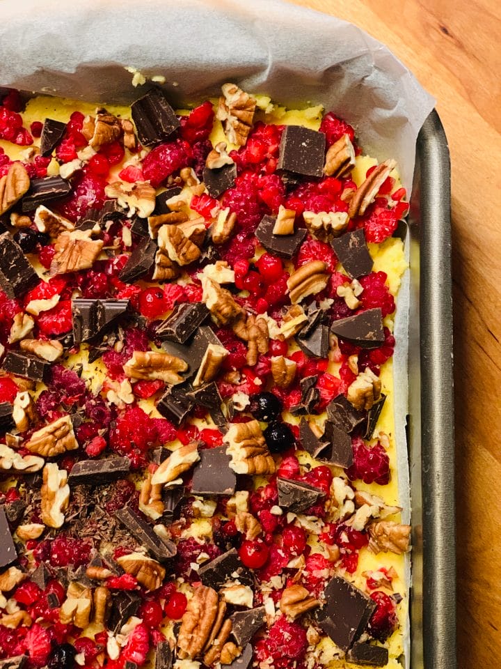 Picture of a keto cake in preparation with chocolate, pecans and raspberries on top, before baking