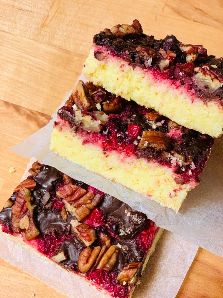 Picture of a keto cake with raspberries, pecans and chocolate on top on a wooden surface