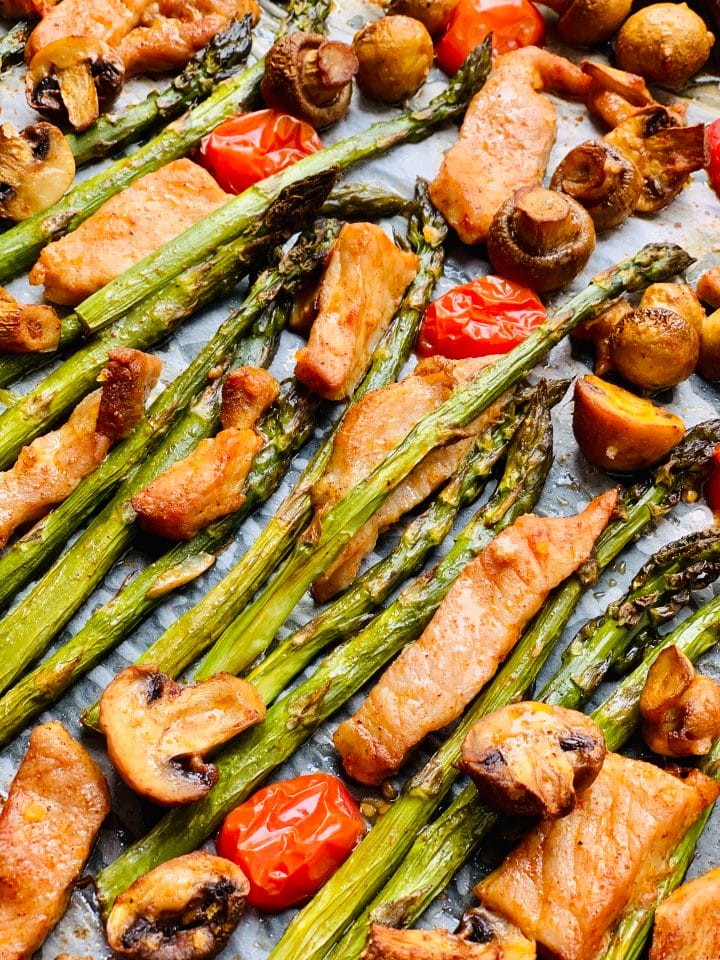 Picture of baked asparagus, pork chops, mushrooms and cherry tomatoes in a baking tray