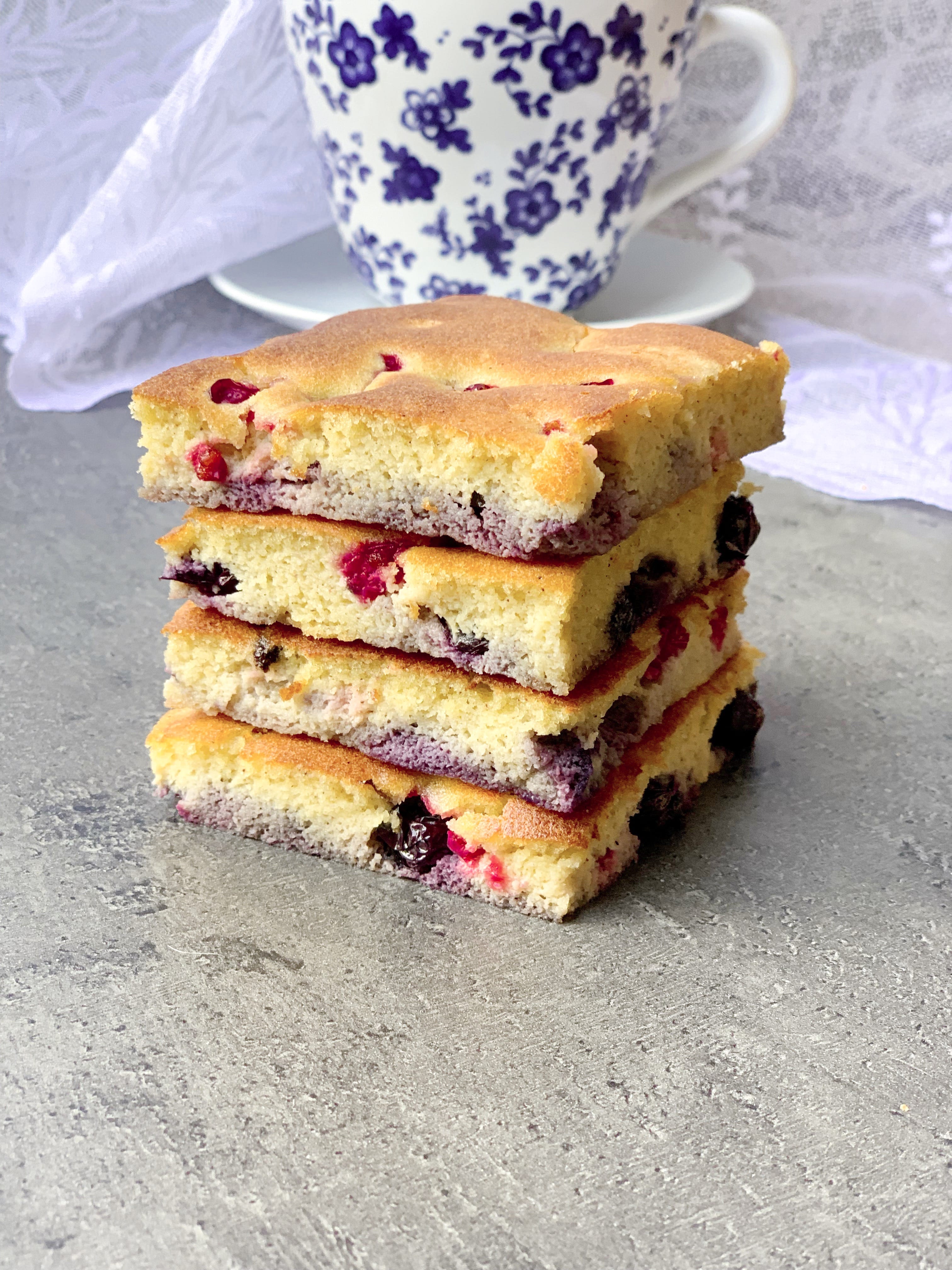 Picture of keto sheet pan pancakes with blueberries and red currants on the table with a cup of tea.