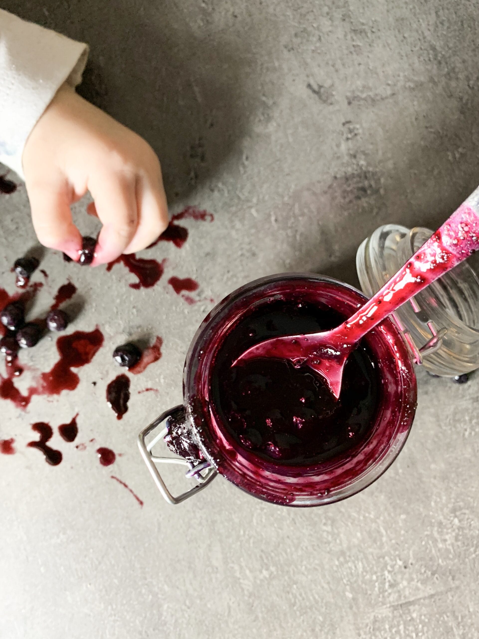 Picture of a baby hand taking a blueberries and keto blueberry jam in jar