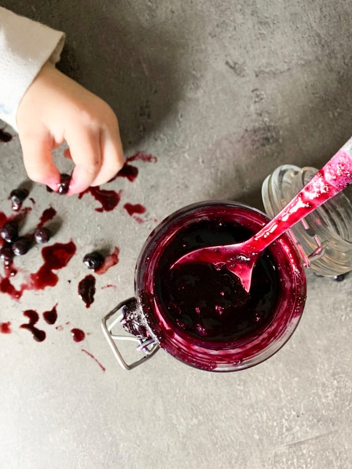 Picture of a baby hand taking a blueberries and keto blueberry jam in jar