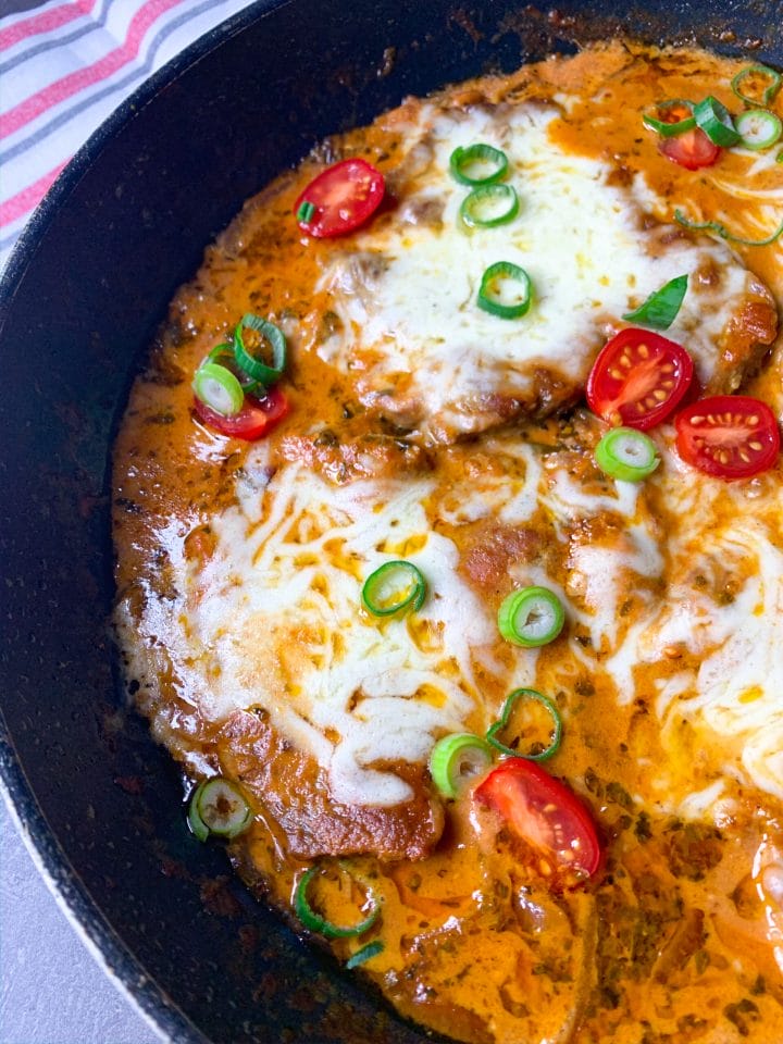 Picture with a skillet with pork neck steak in tomato sauce and mozzarella on top. 