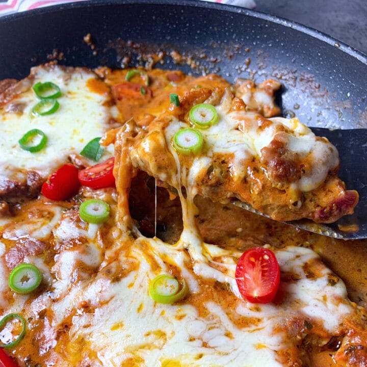 Pork neck with tomato sauce and melted mozzarella in a skillet