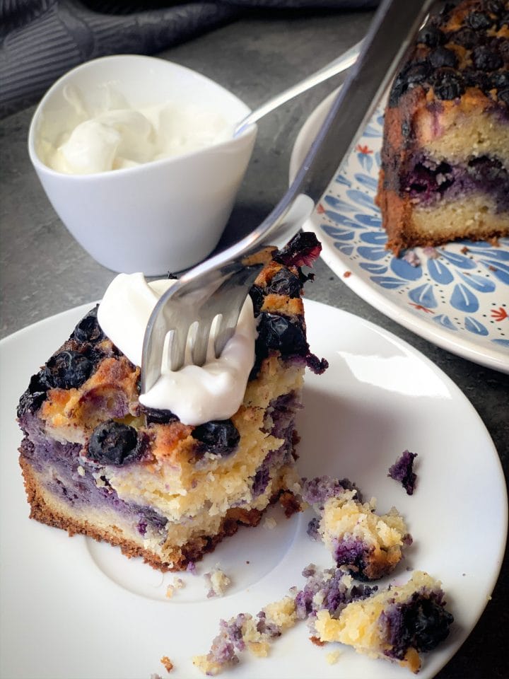 Slice of a keto blueberry cake with a spoon of sour cream on top