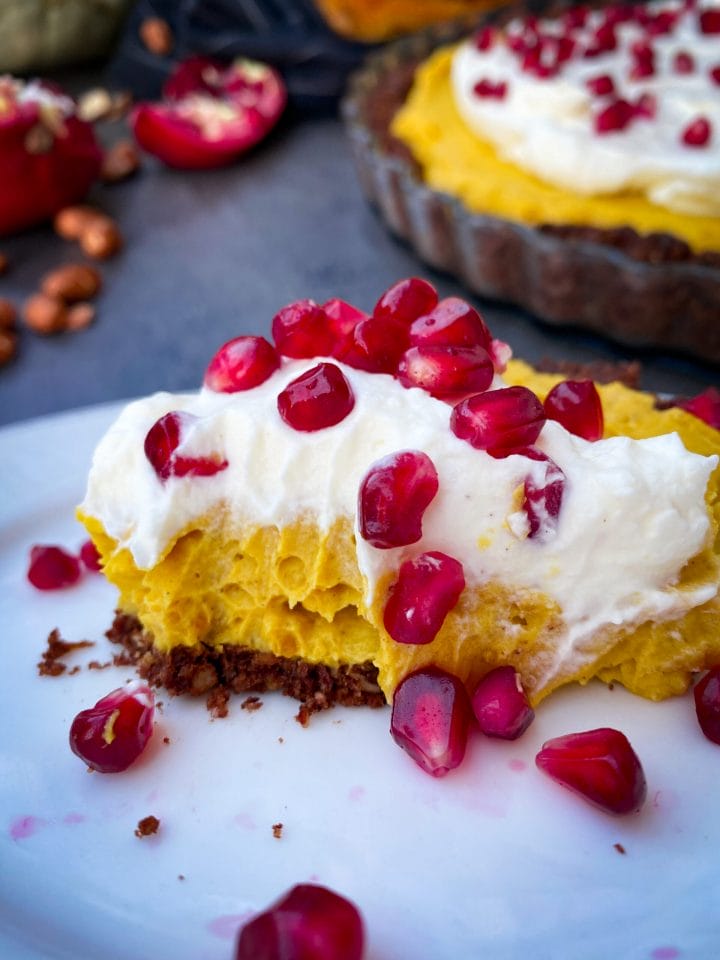 Picture of a slice of pumpkin pie cheesecake with cream on top and pomegranate seeds