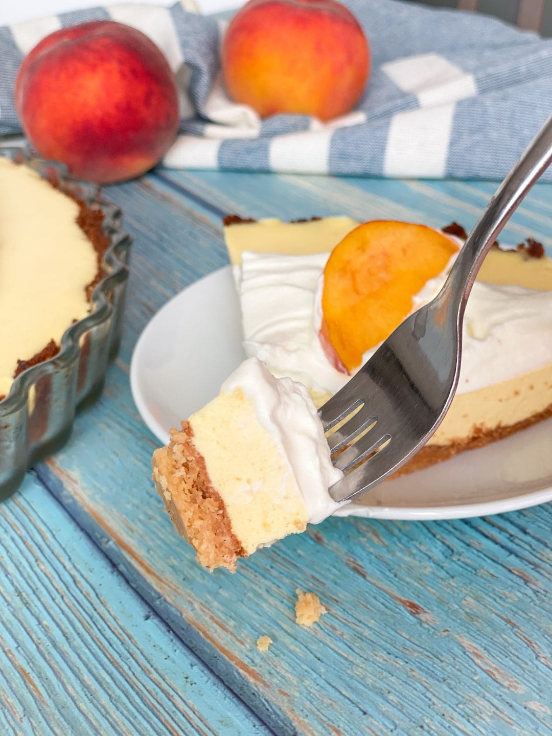 Picture of creamy keto peach pie piece on a fork and a slice of keto peach pie in the back
