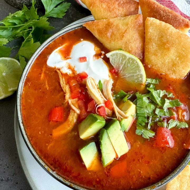 Picture of a bowl of soup with tortilla, avocado and chicken, on the table