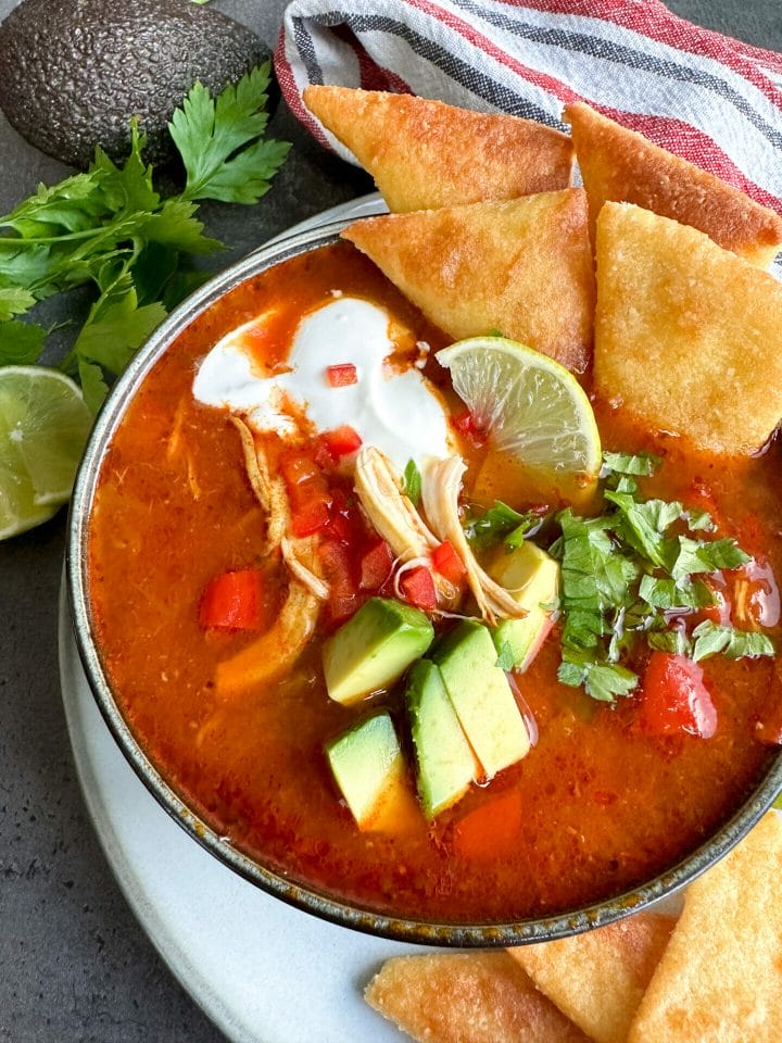 Picture of a bowl of soup with tortilla, avocado and chicken, on the table