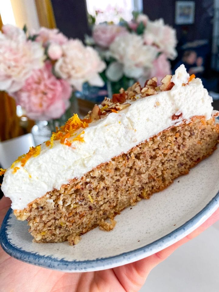 Picture of a slice of keto carrot cake cheesecake with the flowers in the backround.