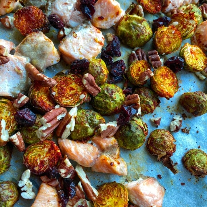 Picture of a salmon and brussel sprouts on a sheet pan baked in the oven with walnuts and cranberries