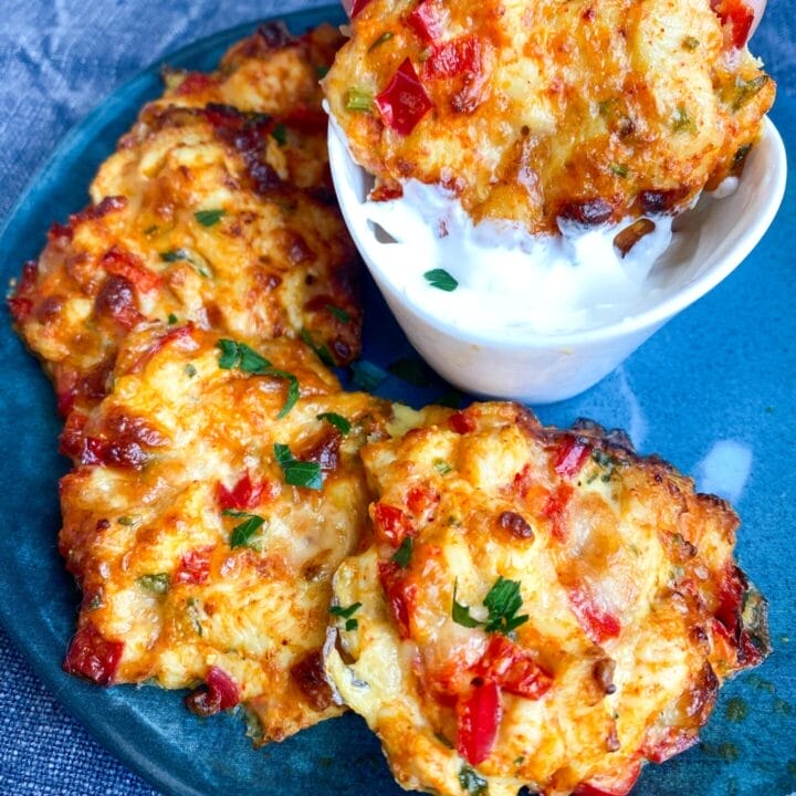 Blue plate with keto cheesy chicken fritters and a little bowl of sour cream dip in the middle.