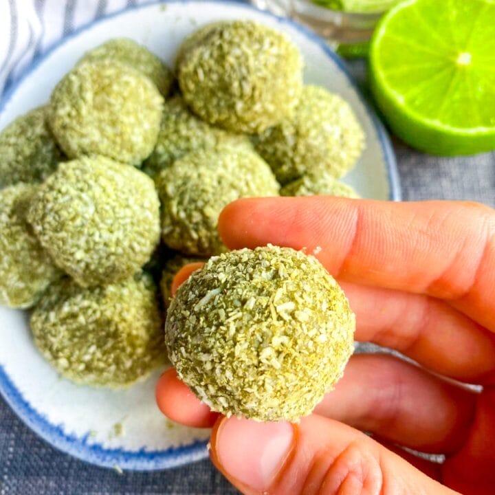 Photo of a plate with keto matcha energy bites in the background and one matcha protein ball in the hand