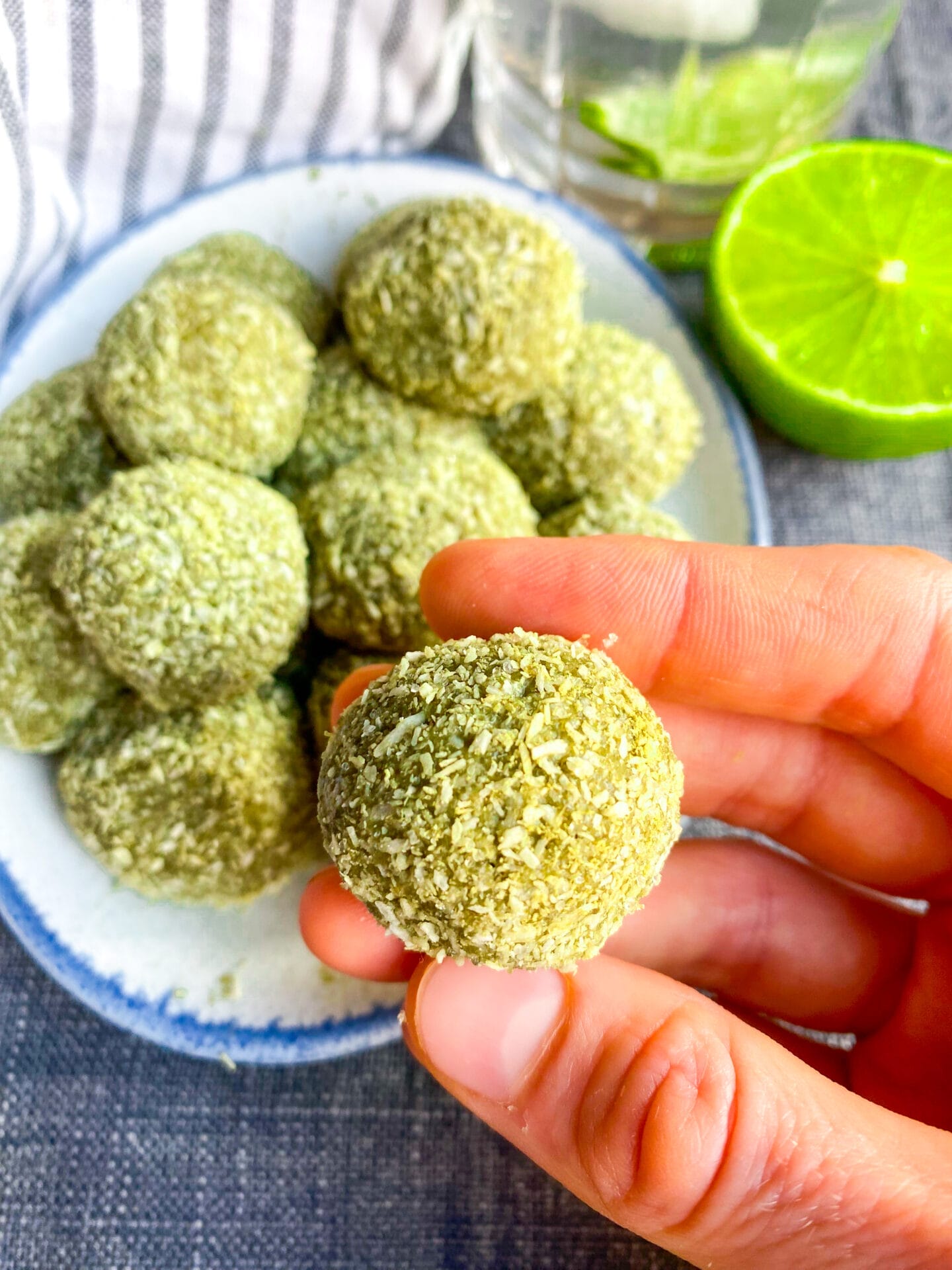 Photo of a plate with keto matcha energy bites in the background and one matcha protein ball in the hand